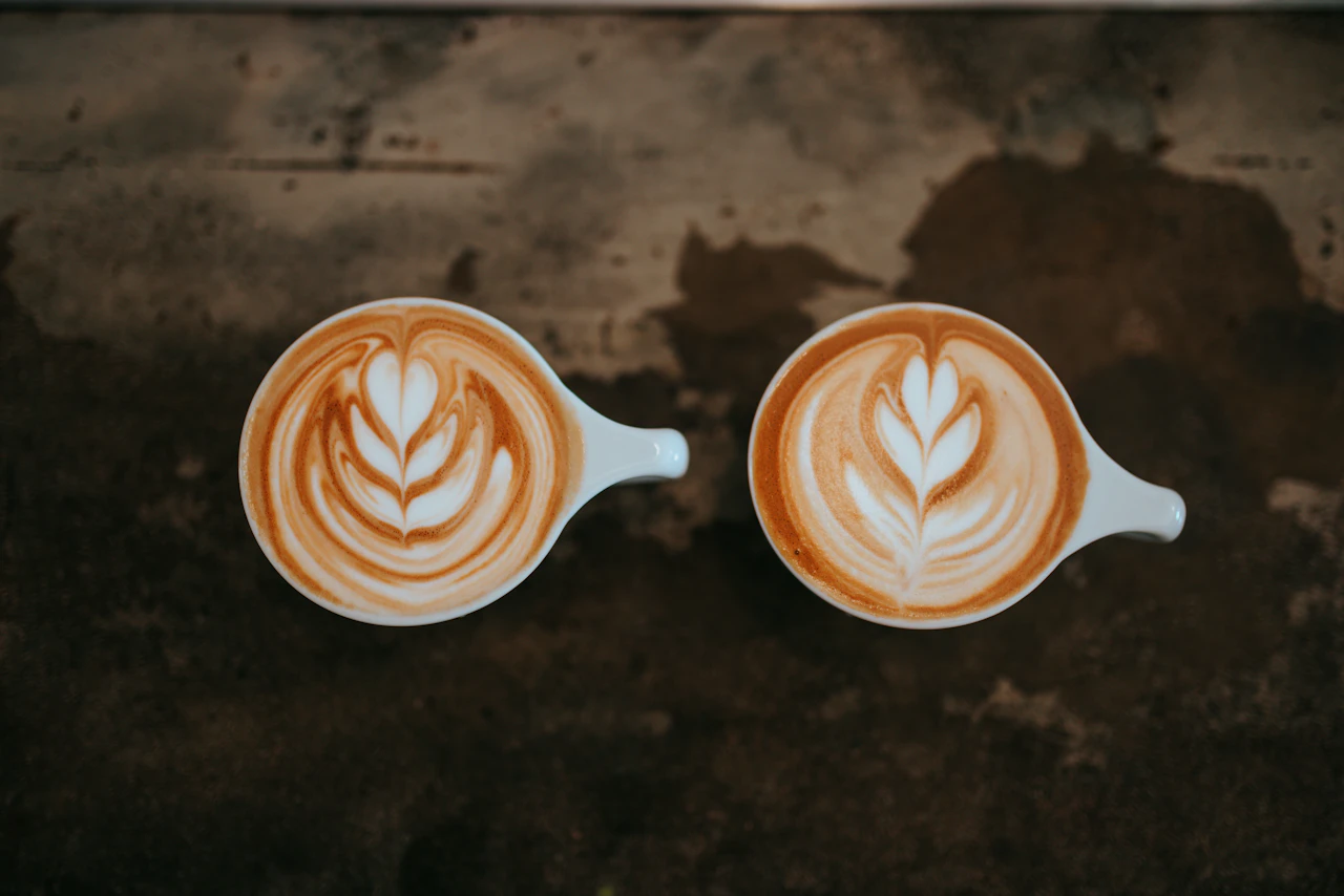 Zwei Tassen mit kunstvoller Latte Art auf einer dunklen Tischplatte.