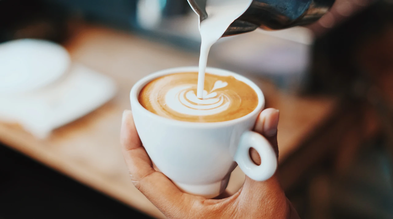 Nahaufnahme von Latte Art, die von Hand in eine Kaffeetasse gegossen wird.