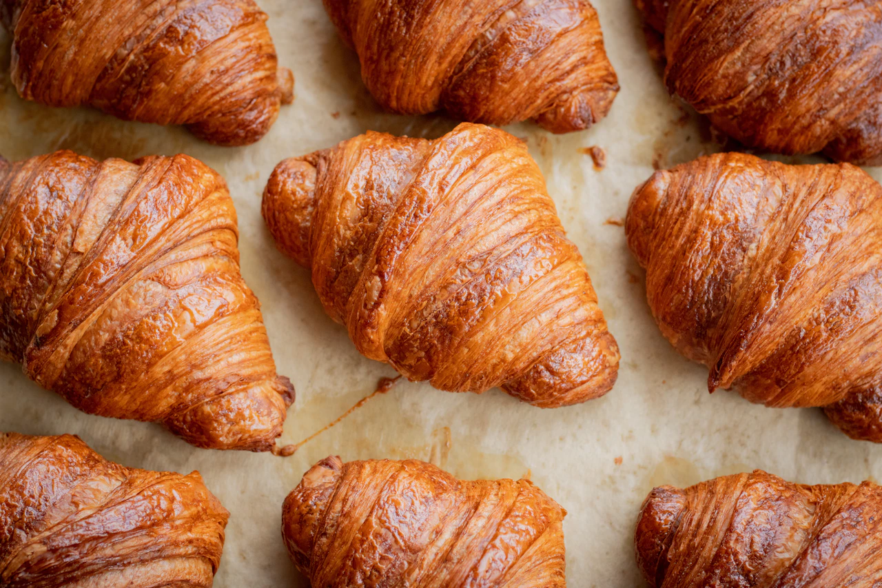 Goldbraun gebackene Buttercroissants auf hellem Backpapier.